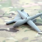 U.S. Sea Drone Strike Marks New Phase In Iran Conflict Small gray drone model on camouflage fabric
