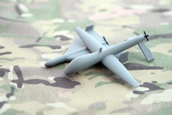 Unnamed,Grey,Toy,Drones,Models,On,Camouflage,Fabric,Close,Up. Small gray drone model on camouflage fabric