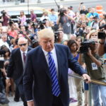 Questions Follow Trump’s Foreign Business Fee A public figure surrounded by a crowd of photographers and onlookers
