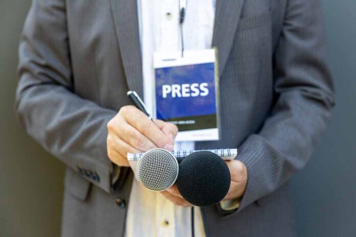 Press member holding microphones and taking notes.