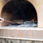 Person cleaning wood-fired oven with brush.