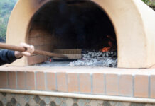 Person cleaning wood-fired oven with brush.