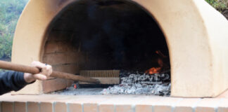 Person cleaning wood-fired oven with brush.