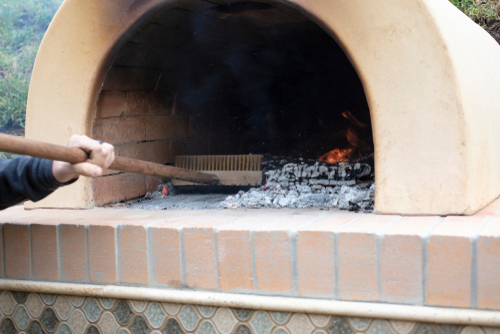 Person cleaning wood-fired oven with brush.