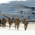 Marines walking away from helicopter on airstrip.