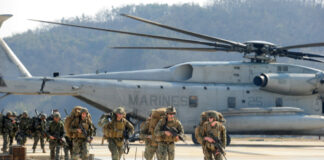 Marines walking away from helicopter on airstrip.