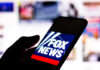 Silhouette hand holding phone displaying Fox News logo.