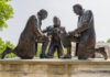 Bronze statues of three men signing a document outdoors.