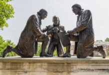 Bronze statues of three men signing a document outdoors.