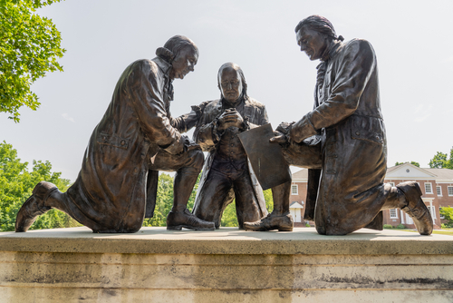 Bronze statues of three men signing a document outdoors.