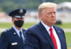 Donald Trump in suit with military personnel behind him.