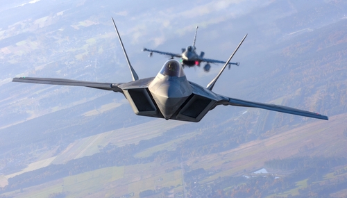 Two fighter jets flying in formation over landscape.