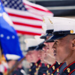 Marines in uniform stand at attention with American flag.