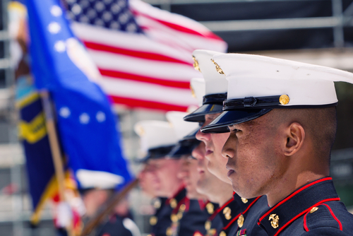 Marines in uniform stand at attention with American flag.