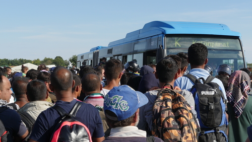 People crowding around blue bus outdoors.