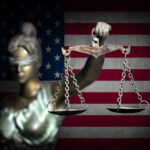 Blindfolded Lady Justice statue with scales, American flag backdrop.